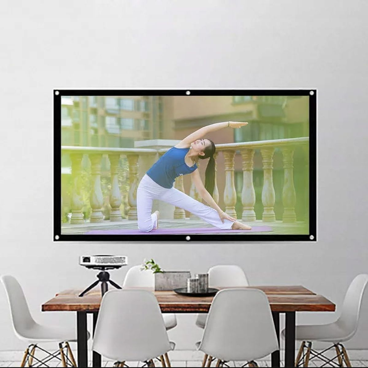 Kobieta uprawiająca jogę na platformie przed białą ścianą, widoczny projektor i krzesła.
