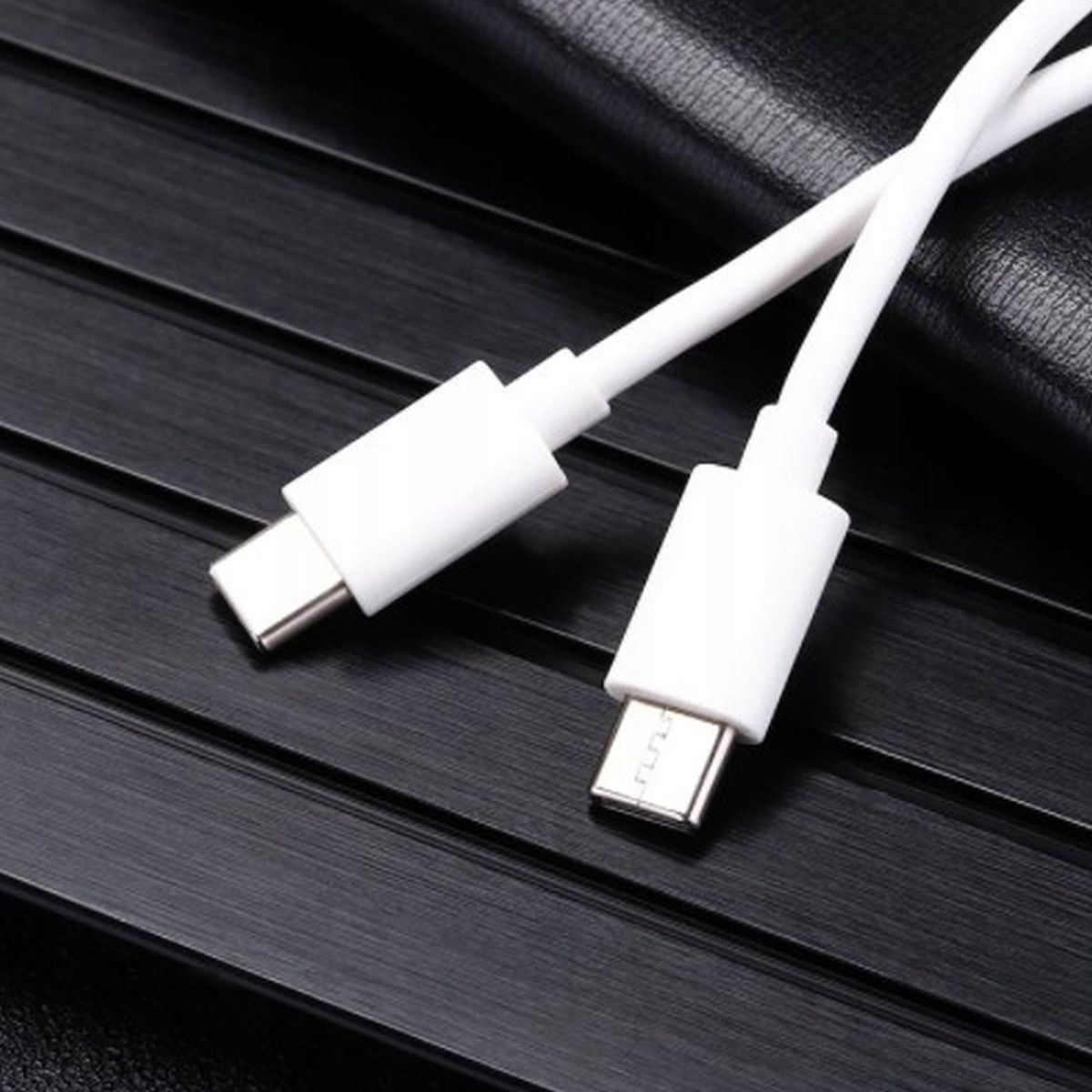 Dwa białe kable USB-C leżące na czarnej, teksturowanej powierzchni.