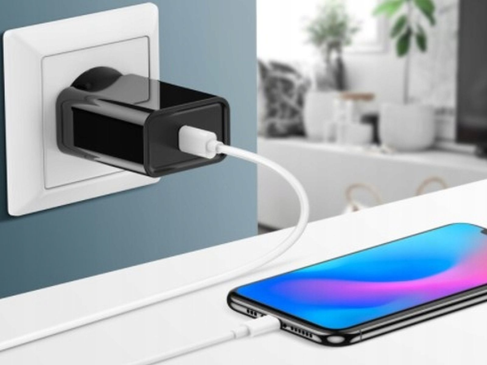 Czarna ładowarka wpięta w białe gniazdko. Telefon jest w pobliżu.