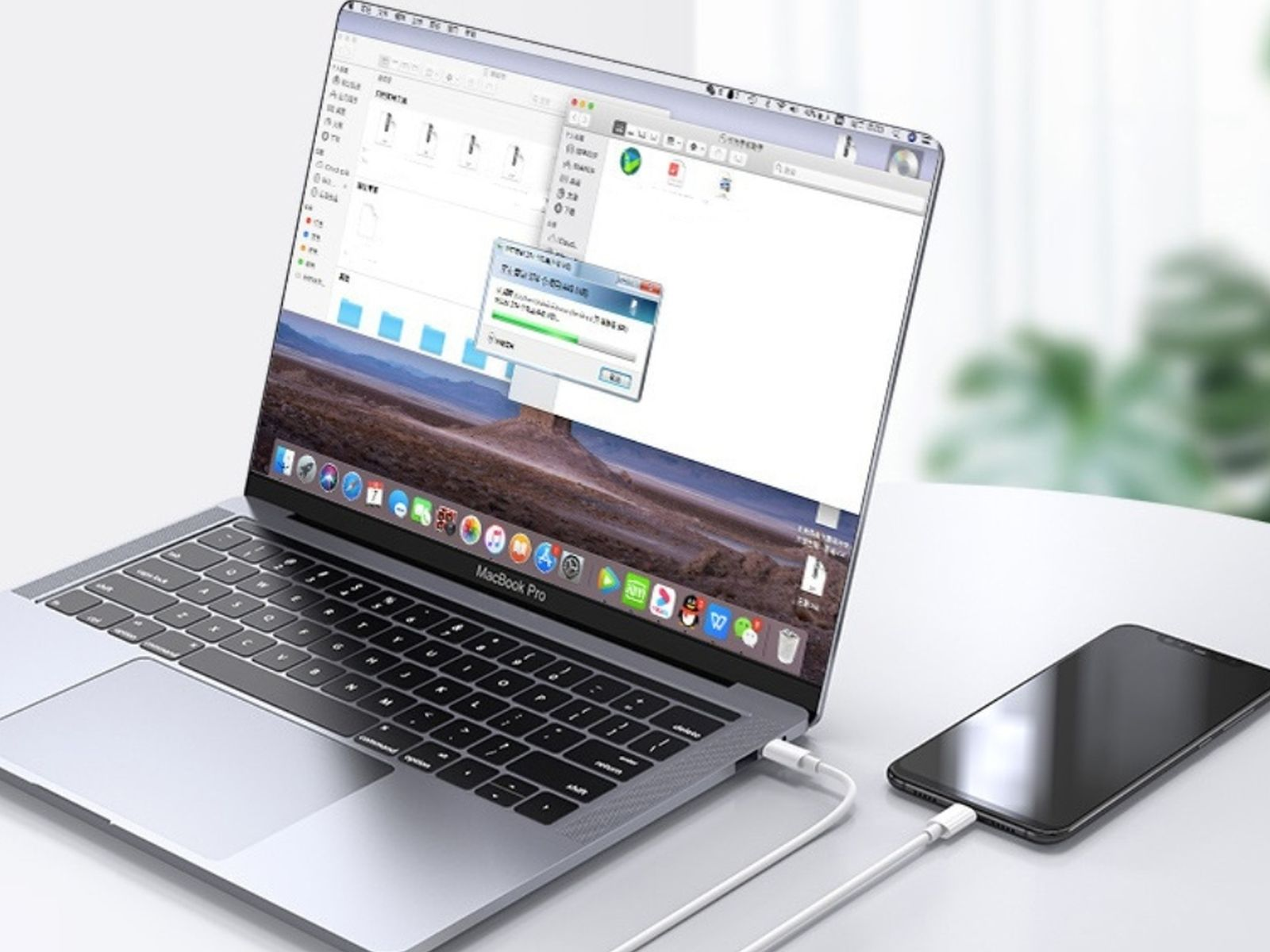 Laptop jest podłączony białym kablem do smartfona. Okno na laptopie pokazuje przesyłanie plików.