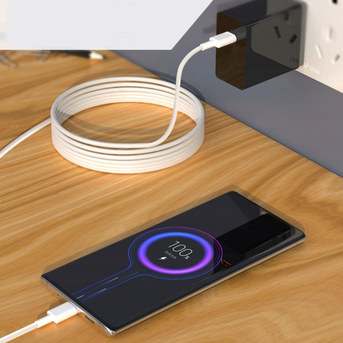 Telefon ładujący się na drewnianym stole. Ekran pokazuje wskaźnik ładowania 100%.