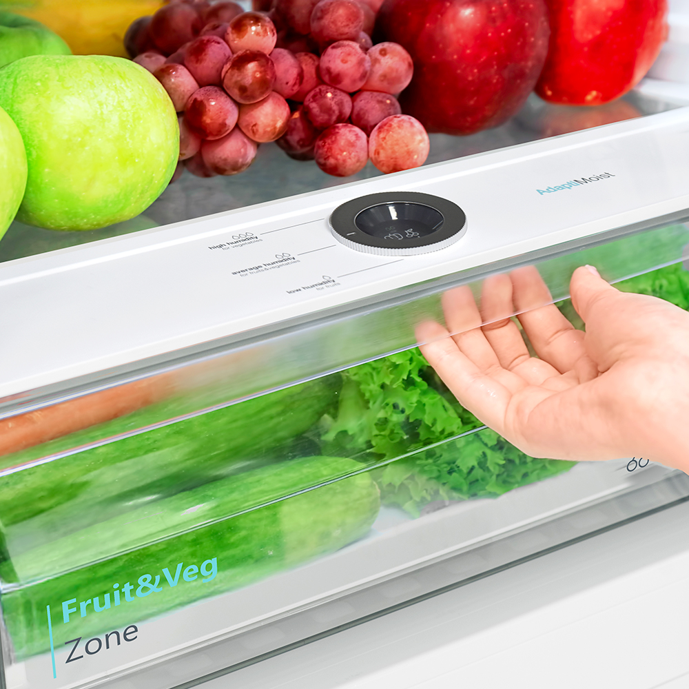 Hand opening a clear drawer in a refrigerator filled with fruits and vegetables.