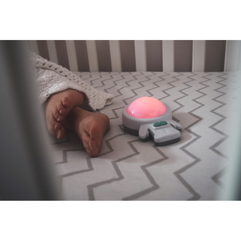Baby im Kinderbett mit einem grau-weißen, Licht emittierenden Spielzeug.