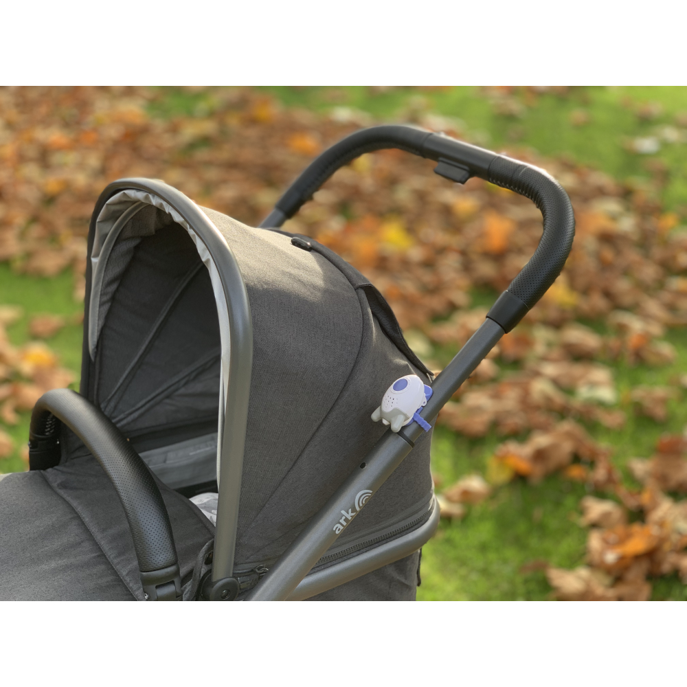 Ein grauer Kinderwagen mit schwarzen Griffen in einem Park mit Herbstlaub.
