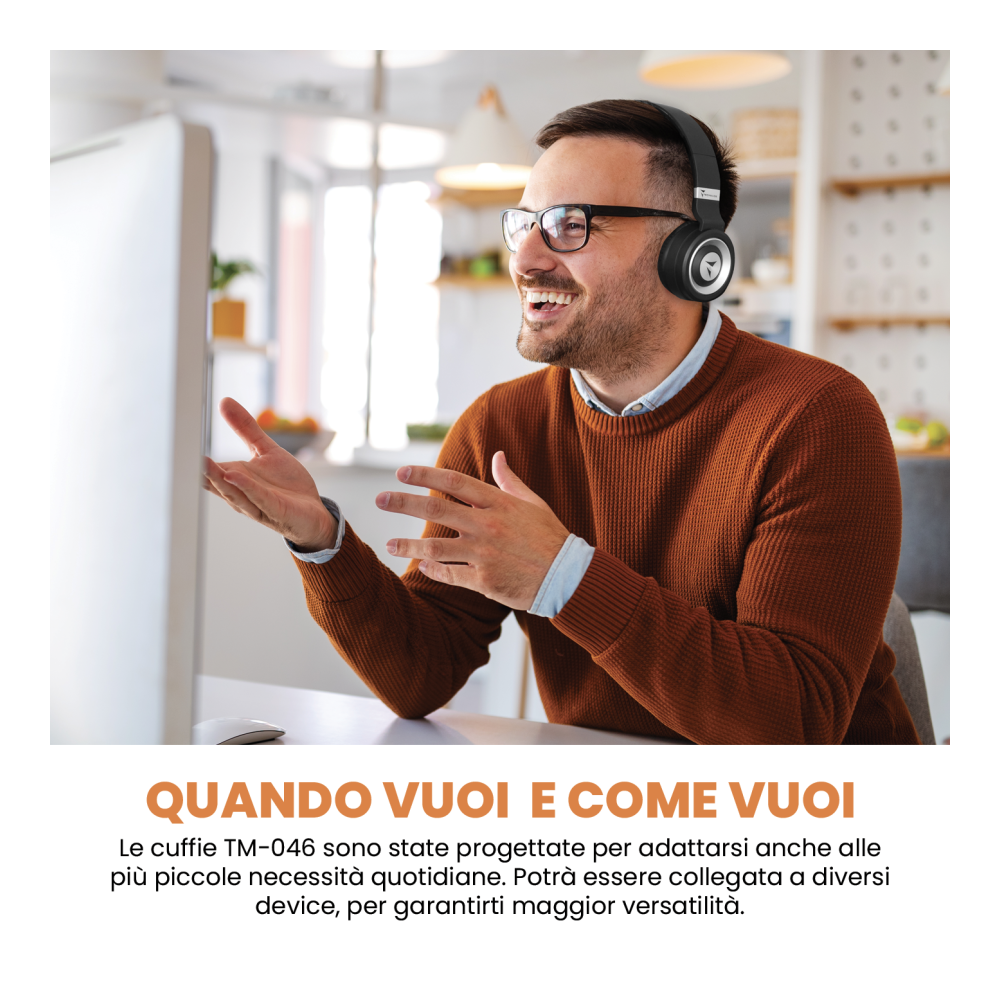 Mann mit Brille und Kopfhörern lächelt, gestikuliert mit den Händen. Weißer Schreibtisch, Computerbildschirm und ein orangefarbener Pullover.