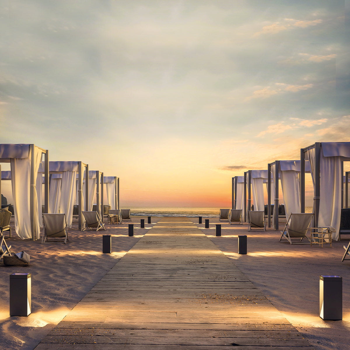 Strandszene bei Sonnenuntergang. Holzweg führt zum Meer. Cabanas auf jeder Seite mit Lichtern auf dem Weg.