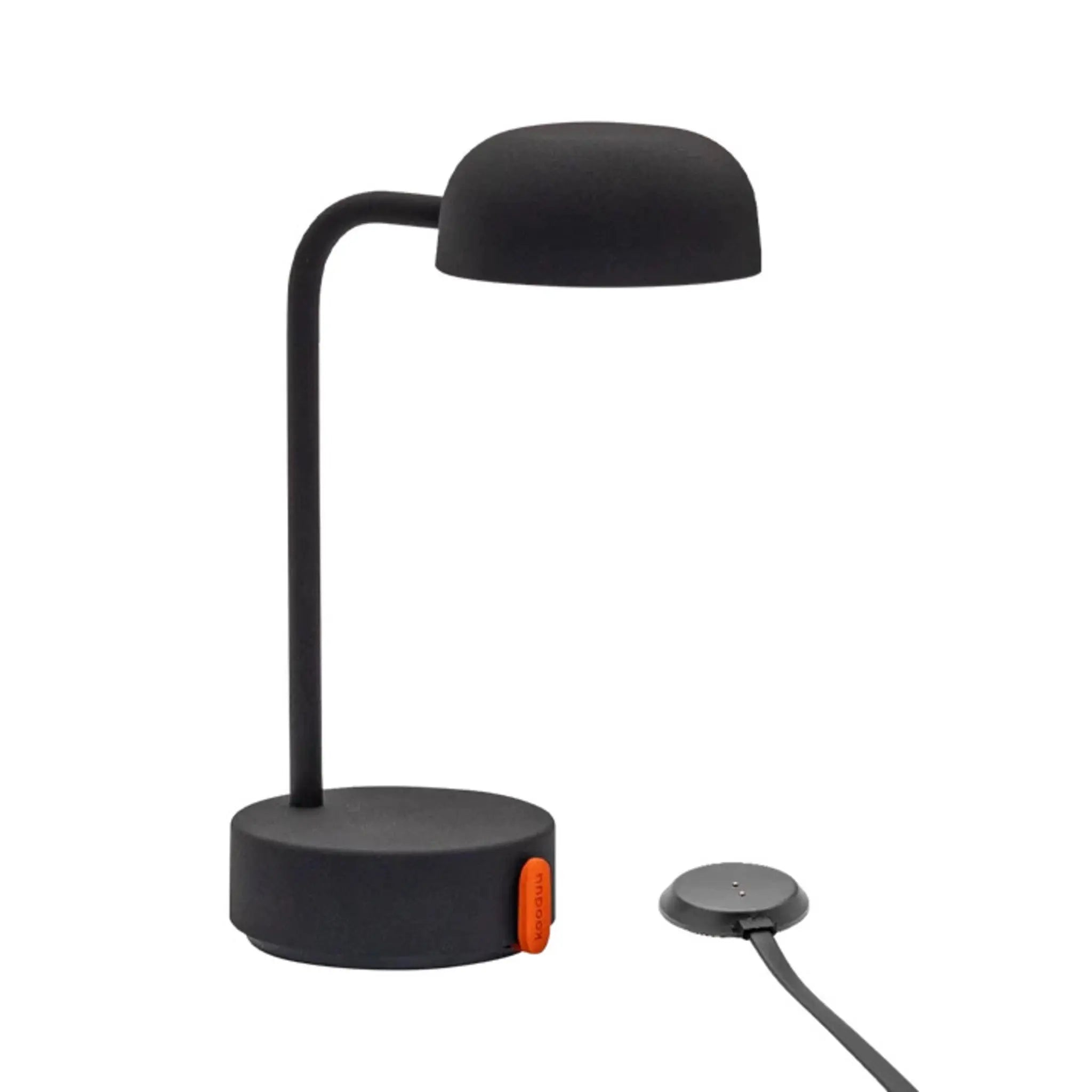 Schwarze Schreibtischlampe mit rundem Oberteil und rundem Sockel. Orangefarbener Knopf am Sockel. Ladepad rechts.