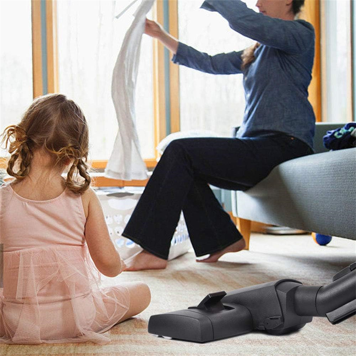 Eine Frau und ein Mädchen in einem Raum, das Mädchen sitzt auf dem Boden, ein Staubsauger ist sichtbar.