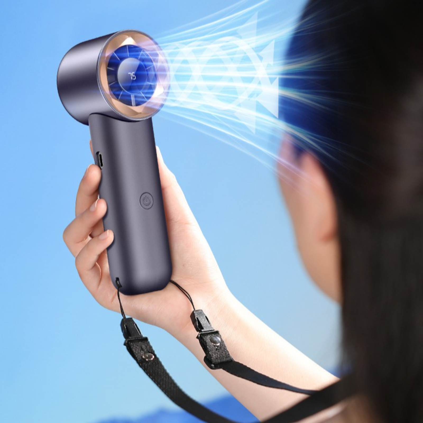 Eine Person hält einen grauen Handventilator, blauer Himmel sichtbar.