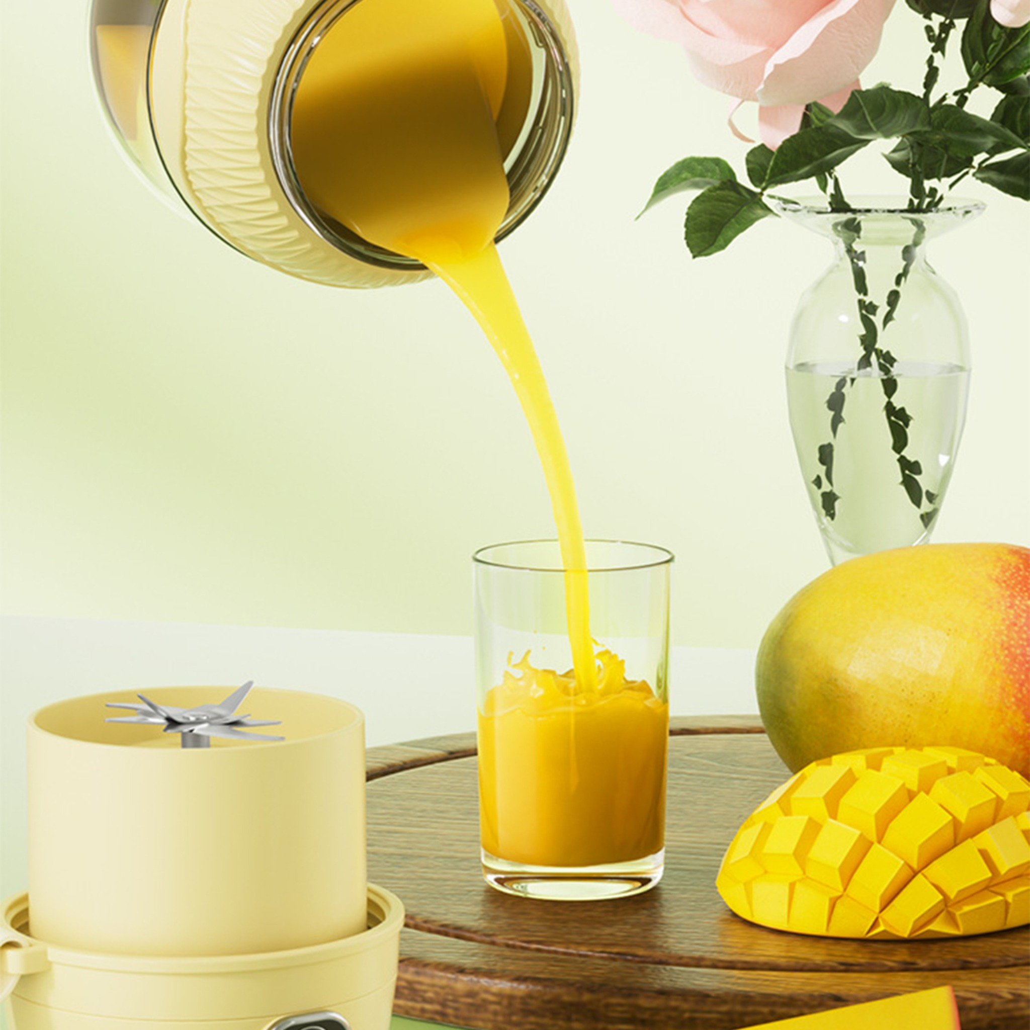 Gelber Saft wird in ein Glas gegossen. Ein Mixer und Mangos stehen daneben. Rosa Blumen und eine Vase sind hinten.