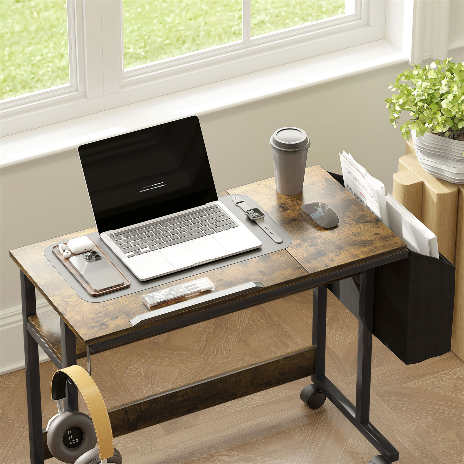 Ein Schreibtisch mit Laptop, Telefon, Maus und Kaffeetasse. Ein Fenster und Kopfhörer sind sichtbar.