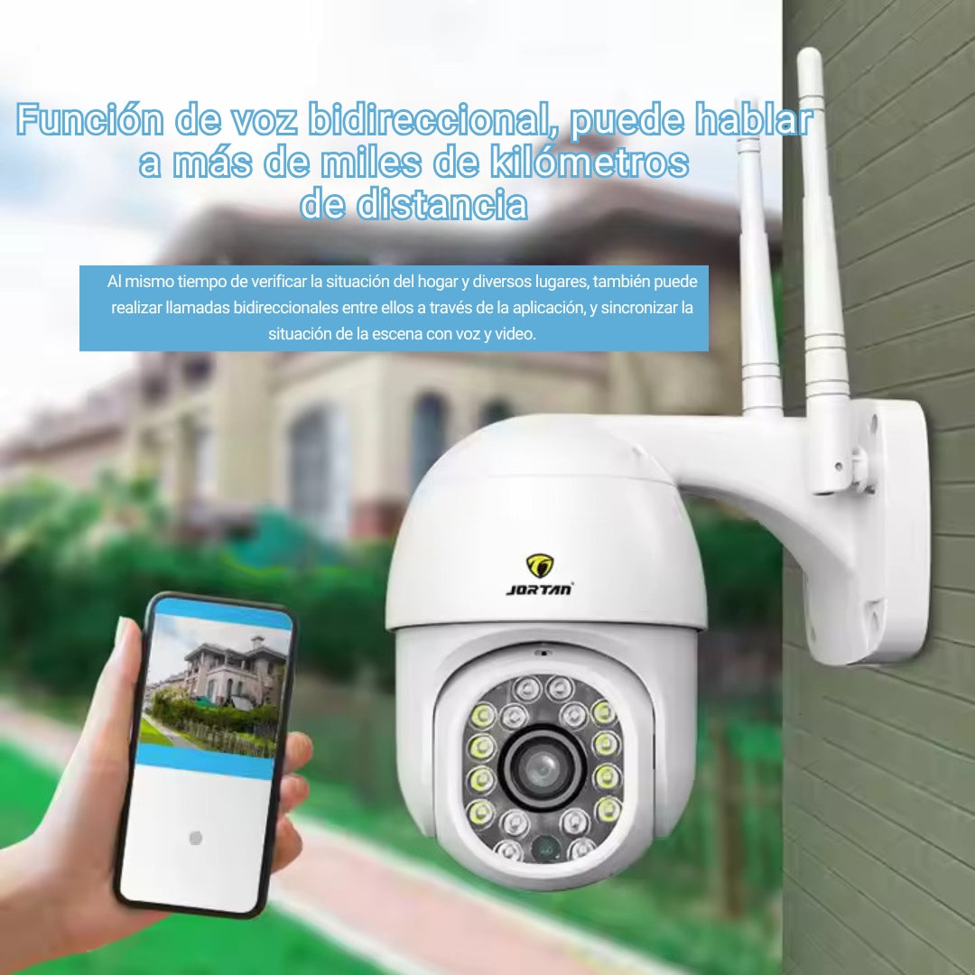Una cámara de seguridad blanca con antenas y un teléfono que muestra la vista de la cámara, al aire libre.