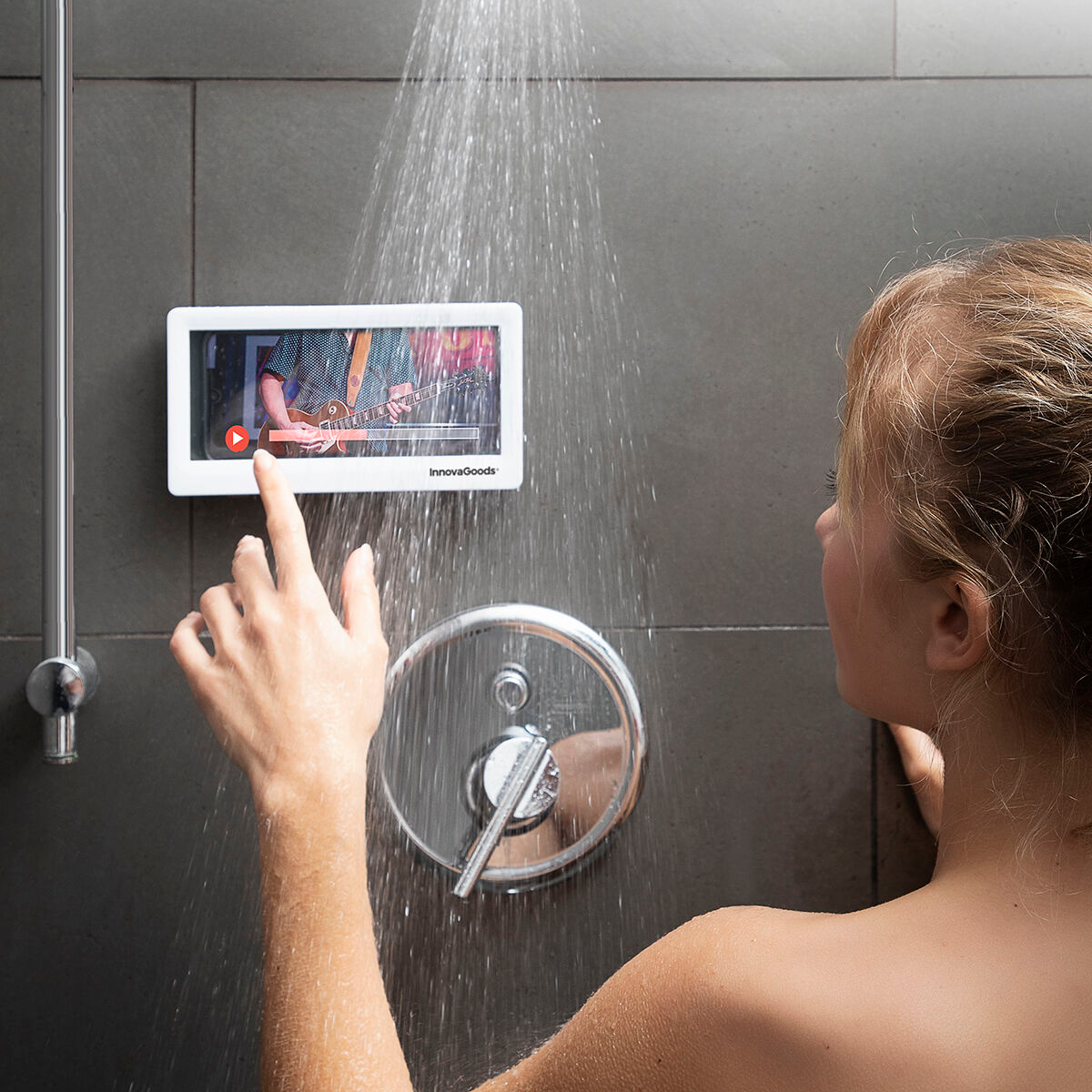 Eine Frau in der Dusche berührt einen Bildschirm, der ein Video eines Gitarristen zeigt.