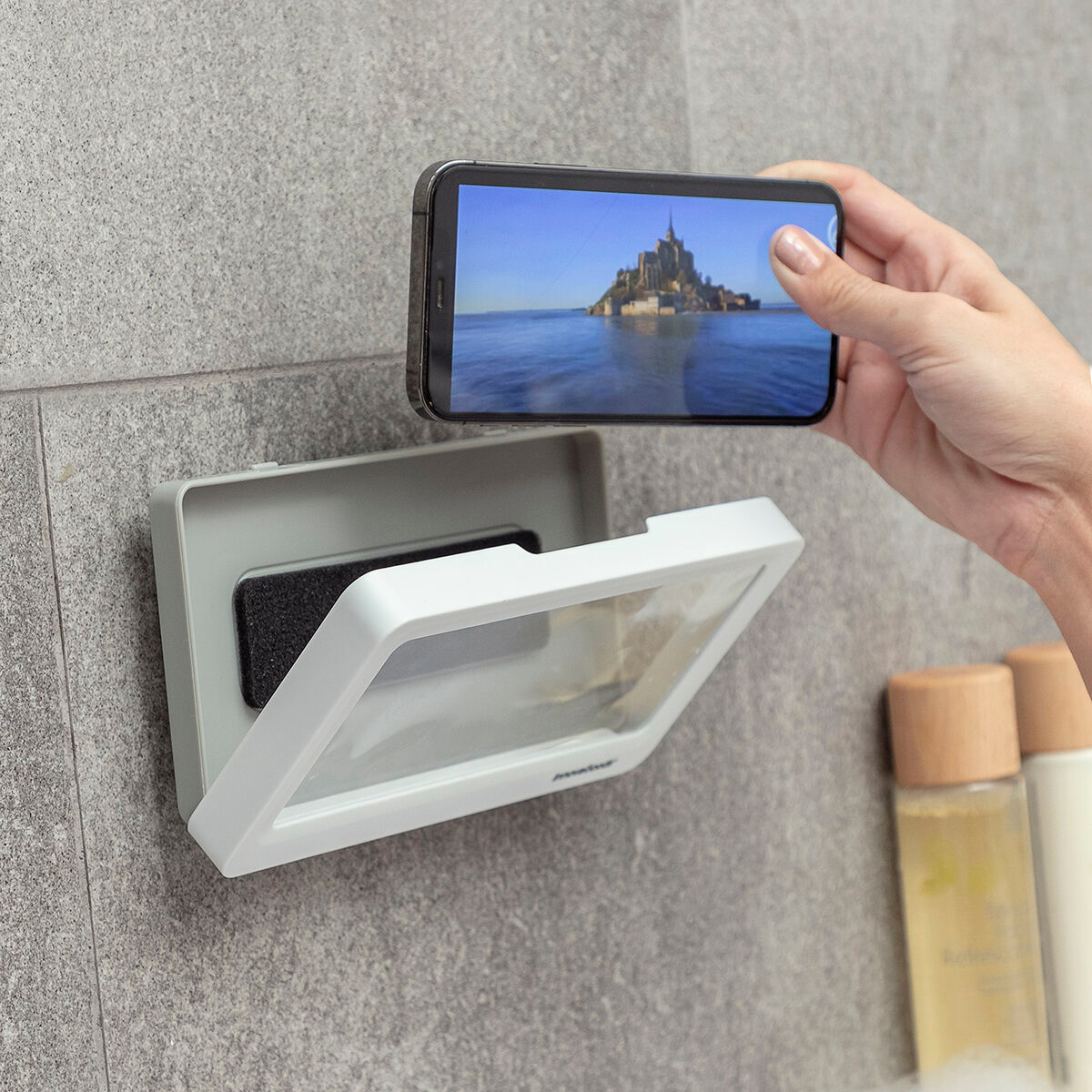 Eine Person hält ein Telefon über eine transparente Duschablage mit einer Burg.