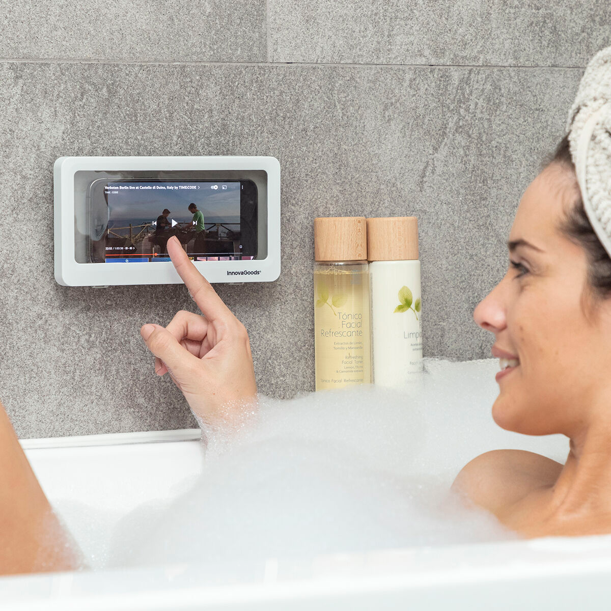 Eine Frau in der Badewanne schaut sich ein Video auf einem Telefon in einer wasserdichten Hülle an.