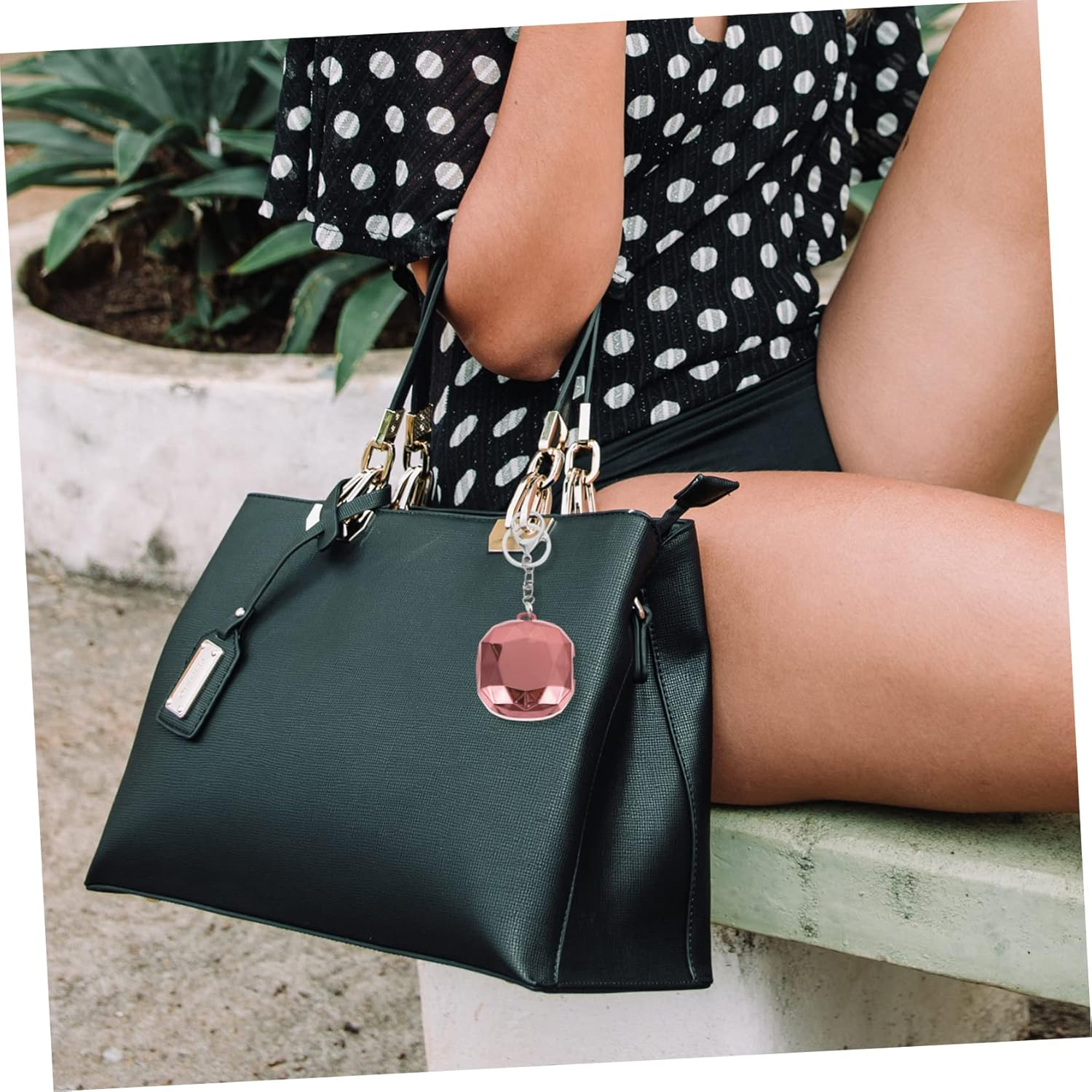 Frau hält schwarze Handtasche mit pinkem Anhänger. Sie trägt gepunktetes Oberteil und Shorts.