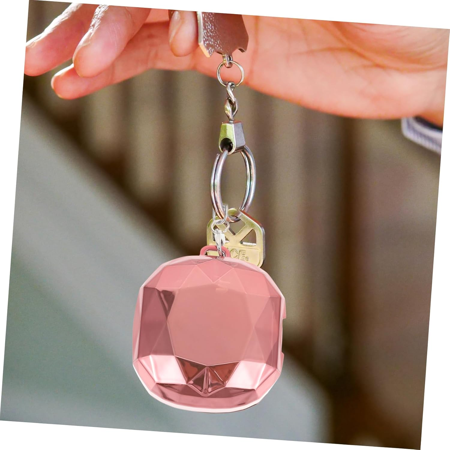 Eine Hand hält einen rosa, juwelenförmigen Schlüsselfinder an einem Schlüsselbund mit Schlüsseln.