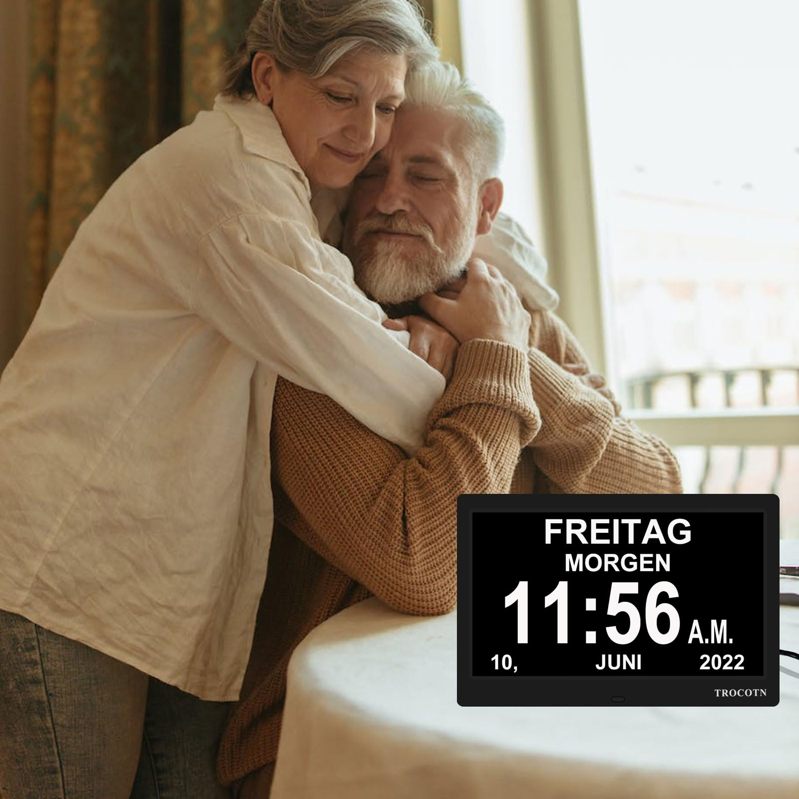 Ein älteres Ehepaar umarmt sich in einem Raum. Eine Digitaluhr zeigt Datum und Uhrzeit: Freitag 11:56 Uhr 2022.