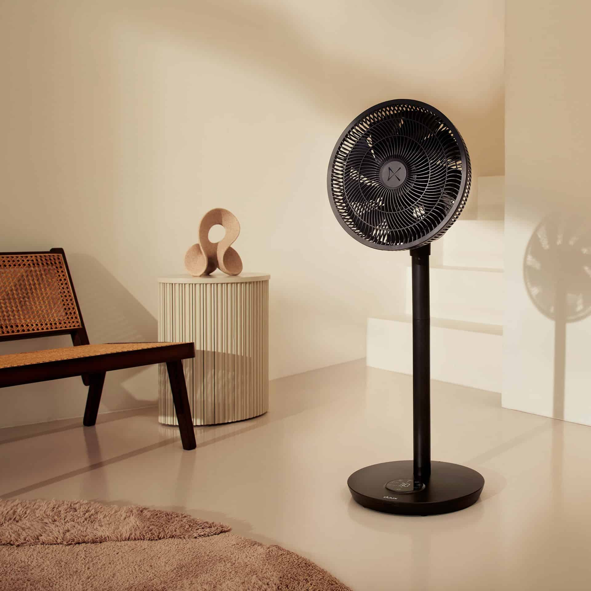 Schwarzer Standventilator in einem Raum mit beigen Wänden, Stuhl, Beistelltisch.