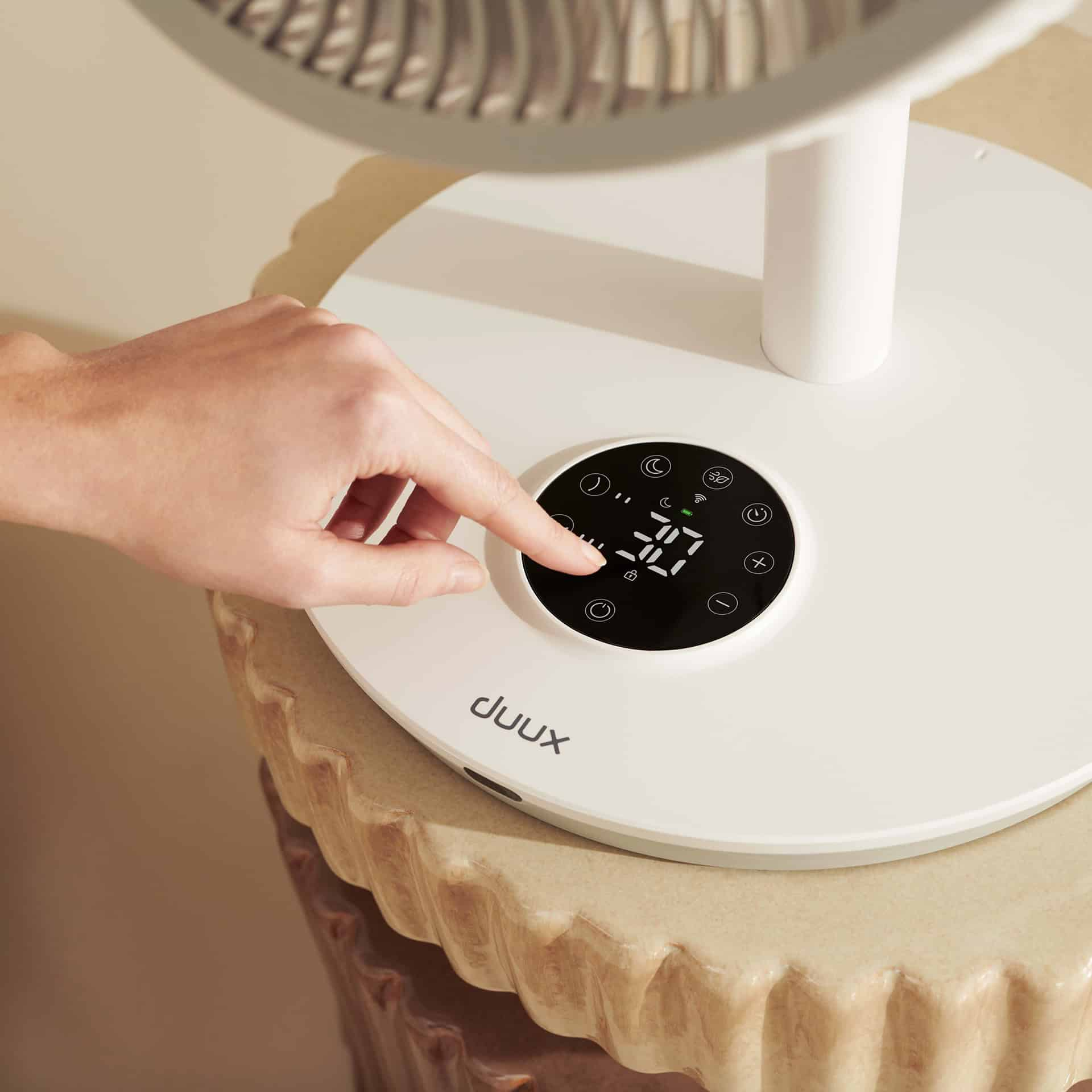 Eine Hand berührt ein Bedienfeld mit digitaler Anzeige an einem weißen Ventilator.