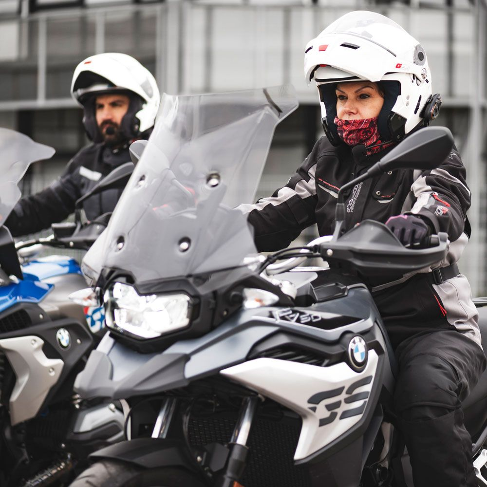 Dwie osoby jadące motocyklami w kaskach i odzieży ochronnej.