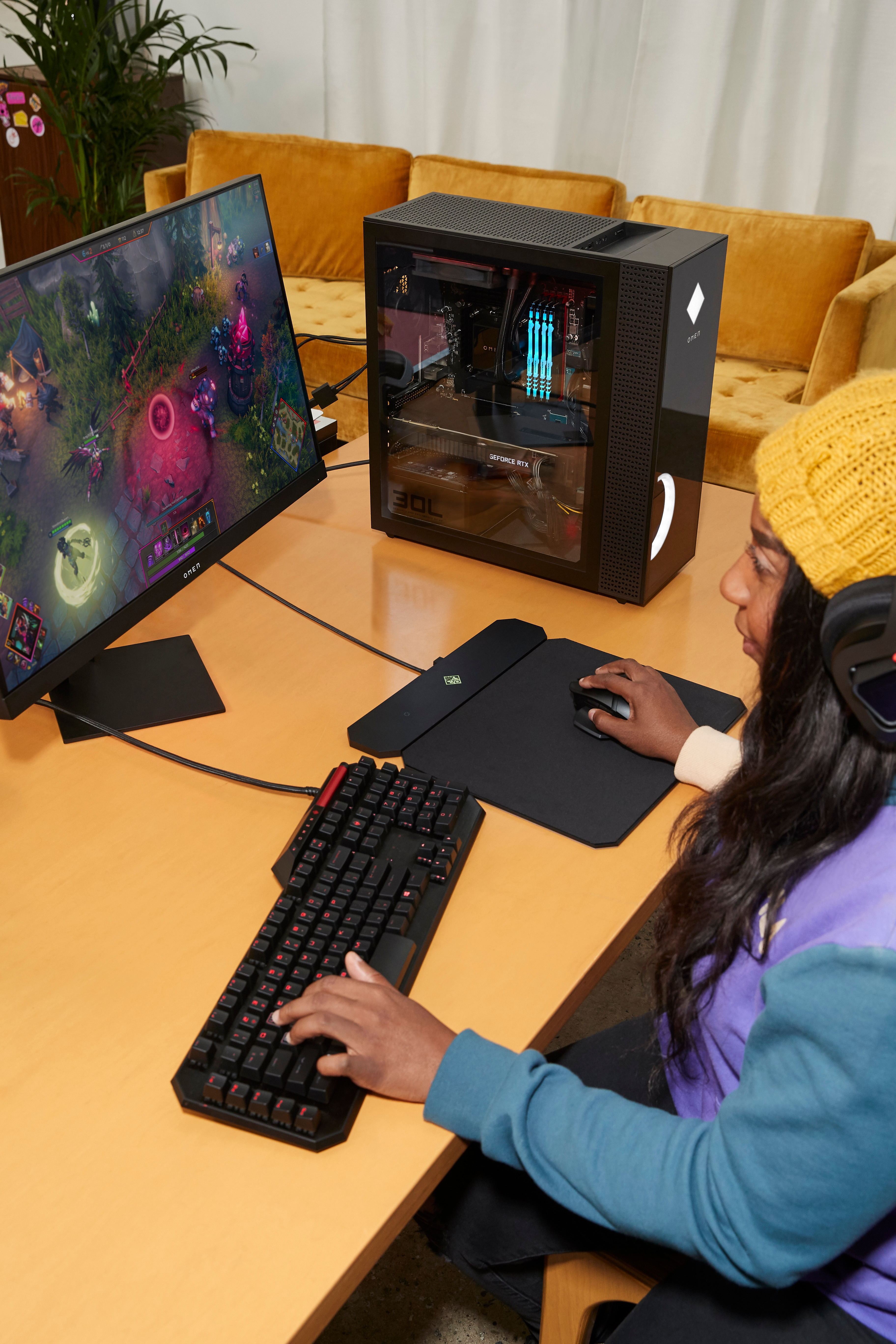 Osoba grająca z konfiguracją PC Omen. Monitor wyświetla grę, klawiaturę i żółty kapelusz.