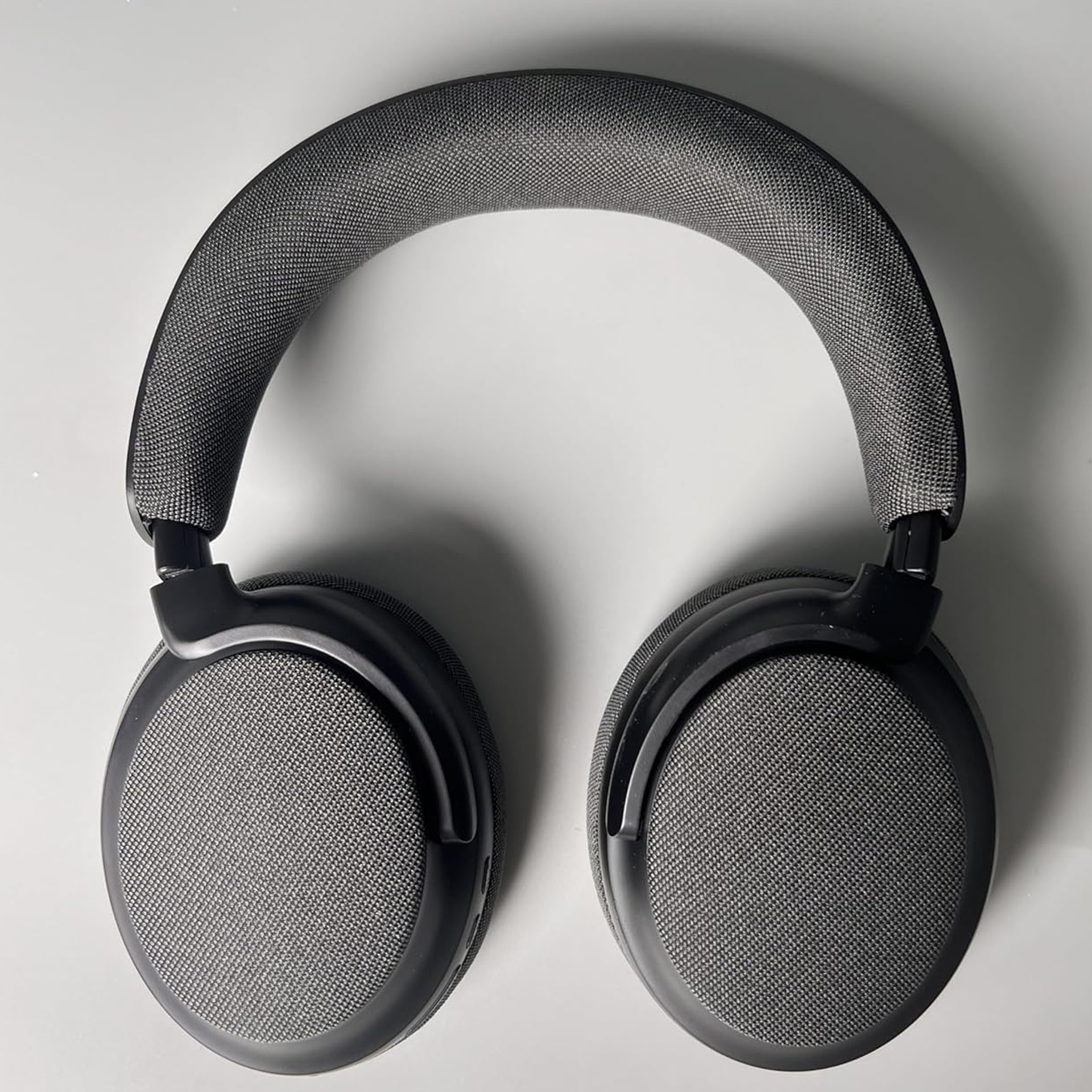 Auriculares supraaurales negros con almohadillas y diadema de malla gris, sobre fondo gris claro.