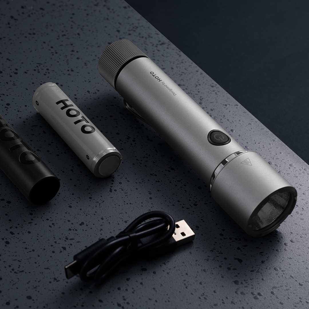 Silberne Taschenlampe, Batterie und USB-Kabel auf dunkler Oberfläche. Die Taschenlampe hat einen Ein-/Ausschalter.