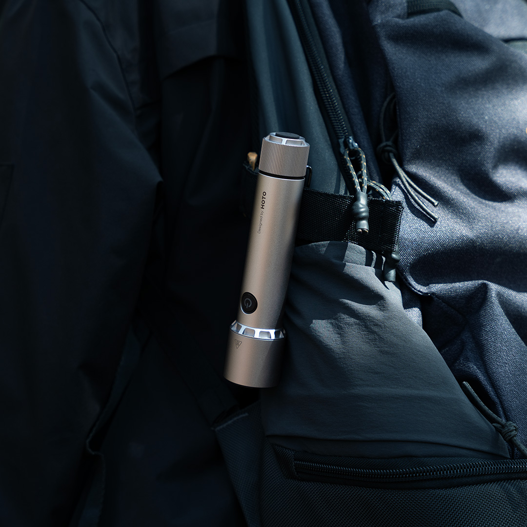 Silberne Taschenlampe an einem dunklen Rucksackriemen befestigt. Schwarzer Hintergrund.