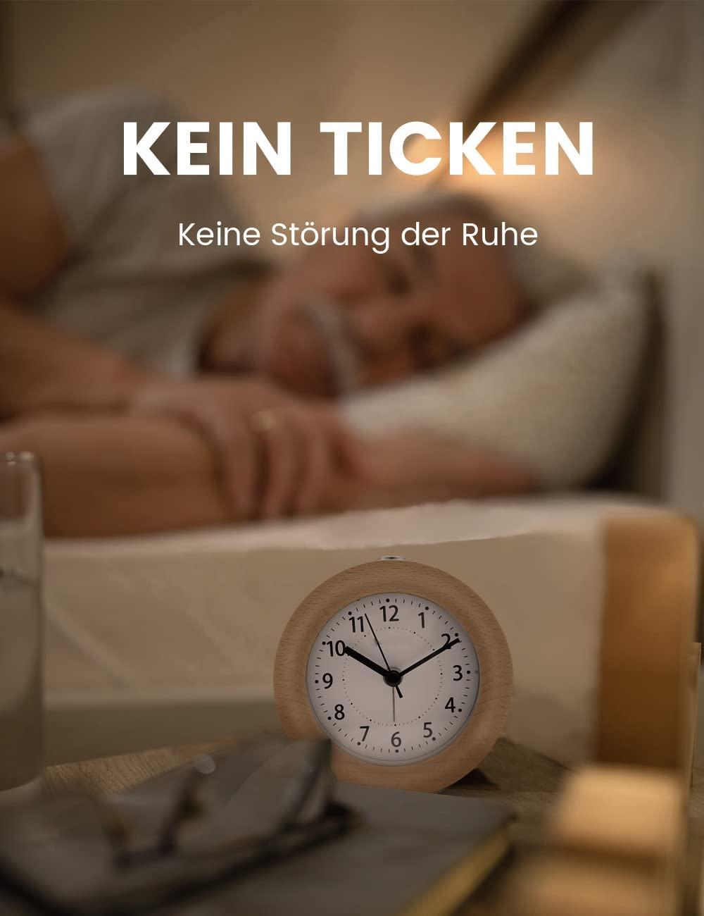 Holzwecker auf Nachttisch, Person im Hintergrund schläft. Text: KEIN TICKEN.
