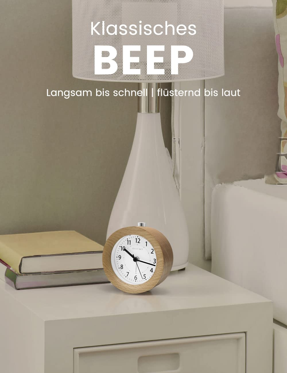Ein klassischer Wecker aus Holz und ein Buch auf einem weißen Nachttisch, mit einer weißen Lampe im Hintergrund.
