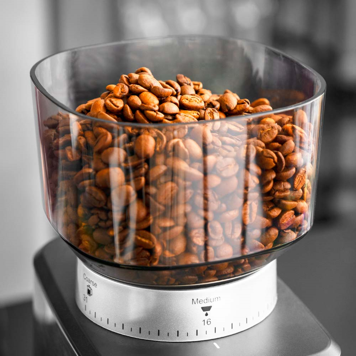 Ein durchsichtiger Behälter ist mit gerösteten Kaffeebohnen gefüllt, die auf einem Kaffeemühlenfuß platziert sind.