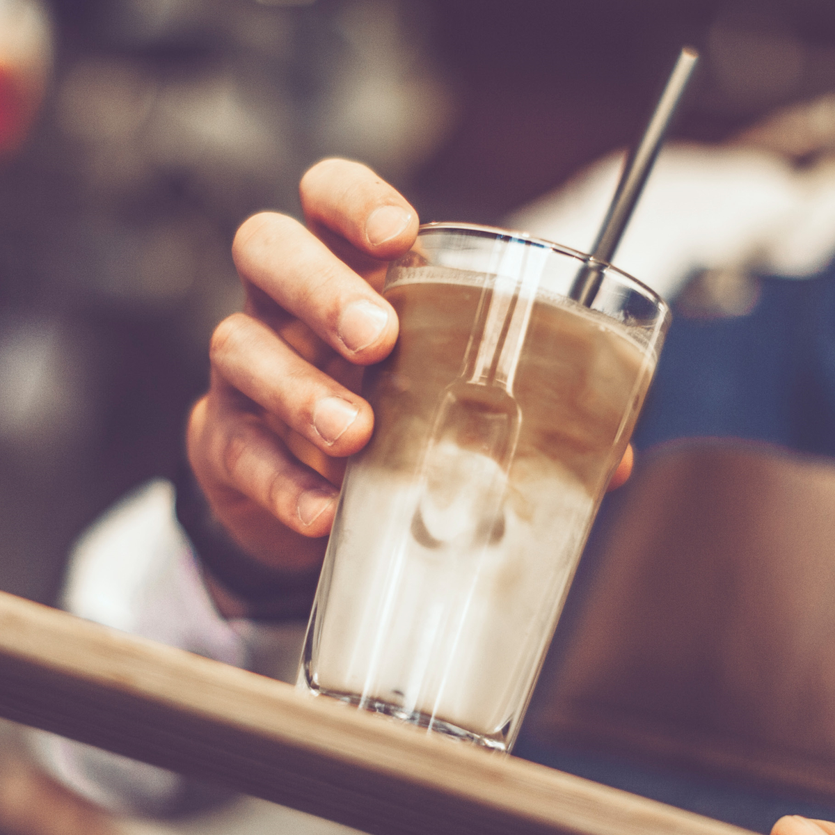 Eine Hand, die ein Glas Latte mit einem Strohhalm in einem Café hält.