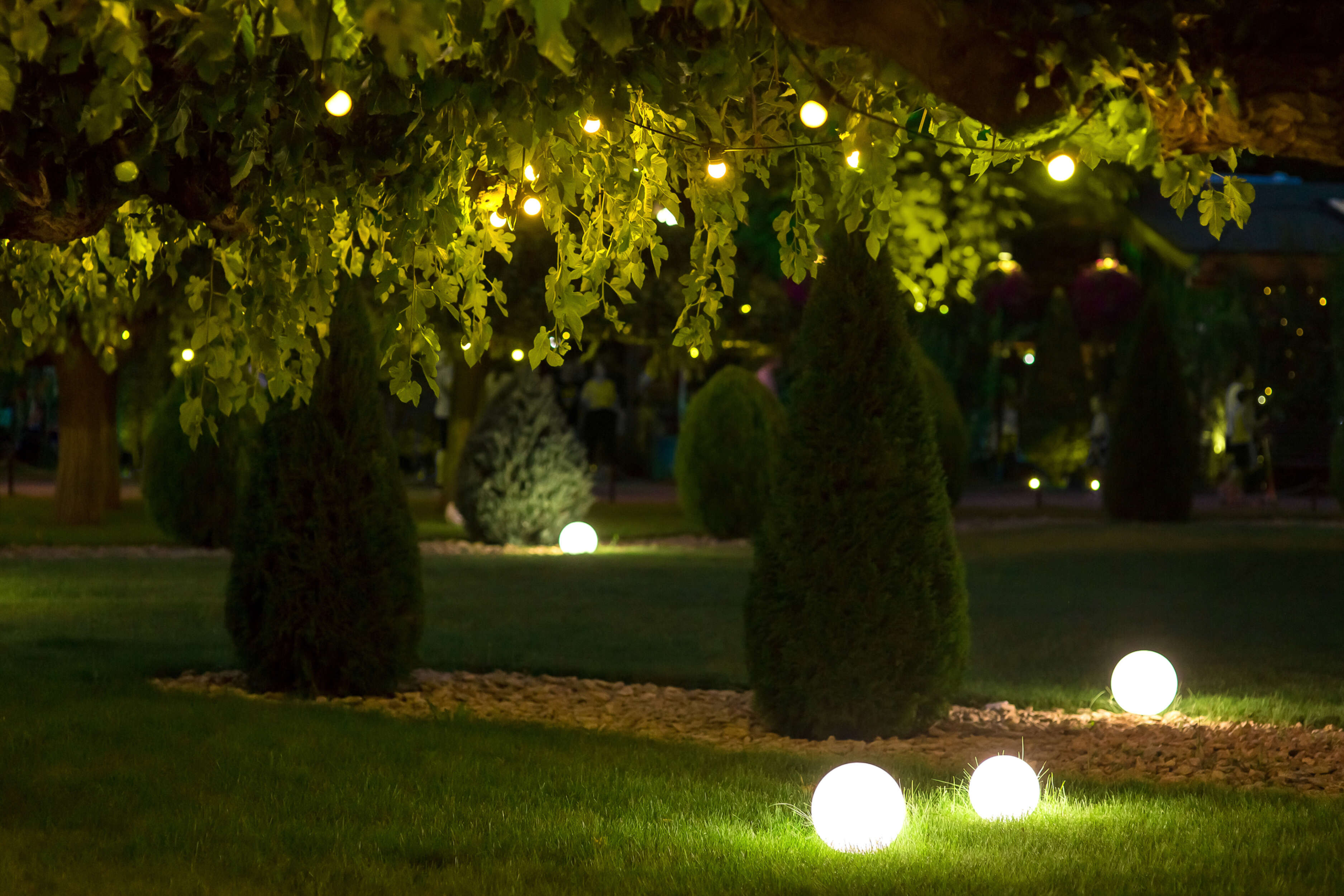 Nachtszenen-Garten mit beleuchteten Kugeln und Lichterketten in Bäumen.