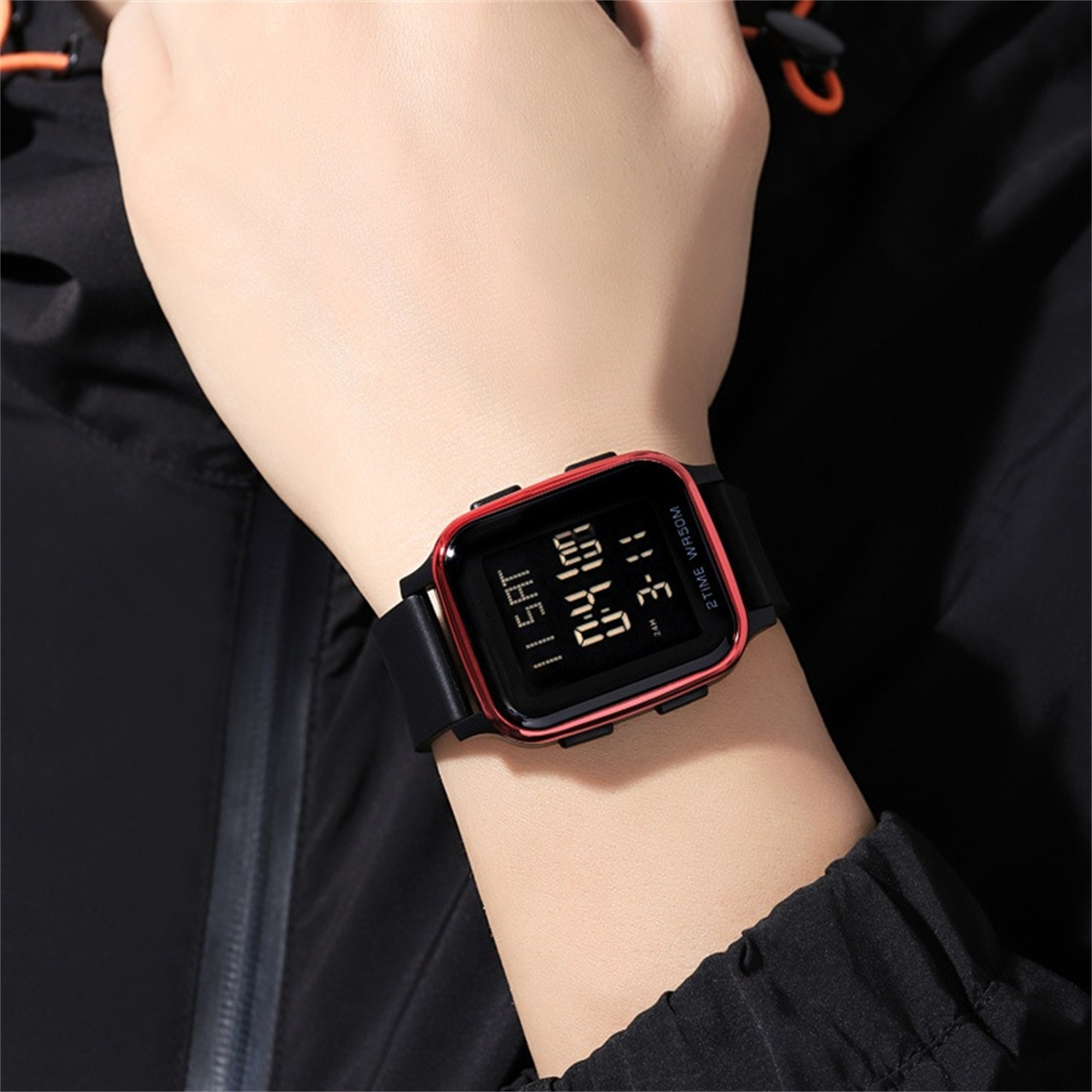 Nahaufnahme eines Handgelenks mit einer schwarzen Digitaluhr. Roter Rahmen, schwarzes Armband, Digitalanzeige.