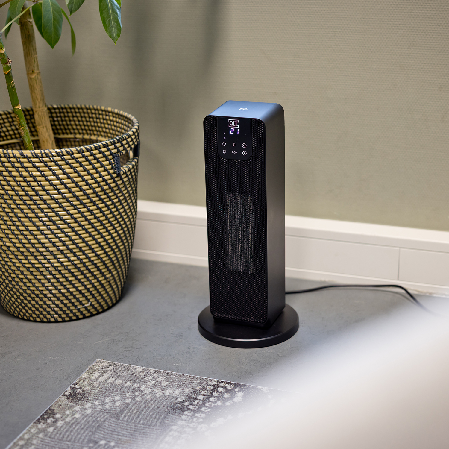 Black electric heater on a round stand, next to a plant.