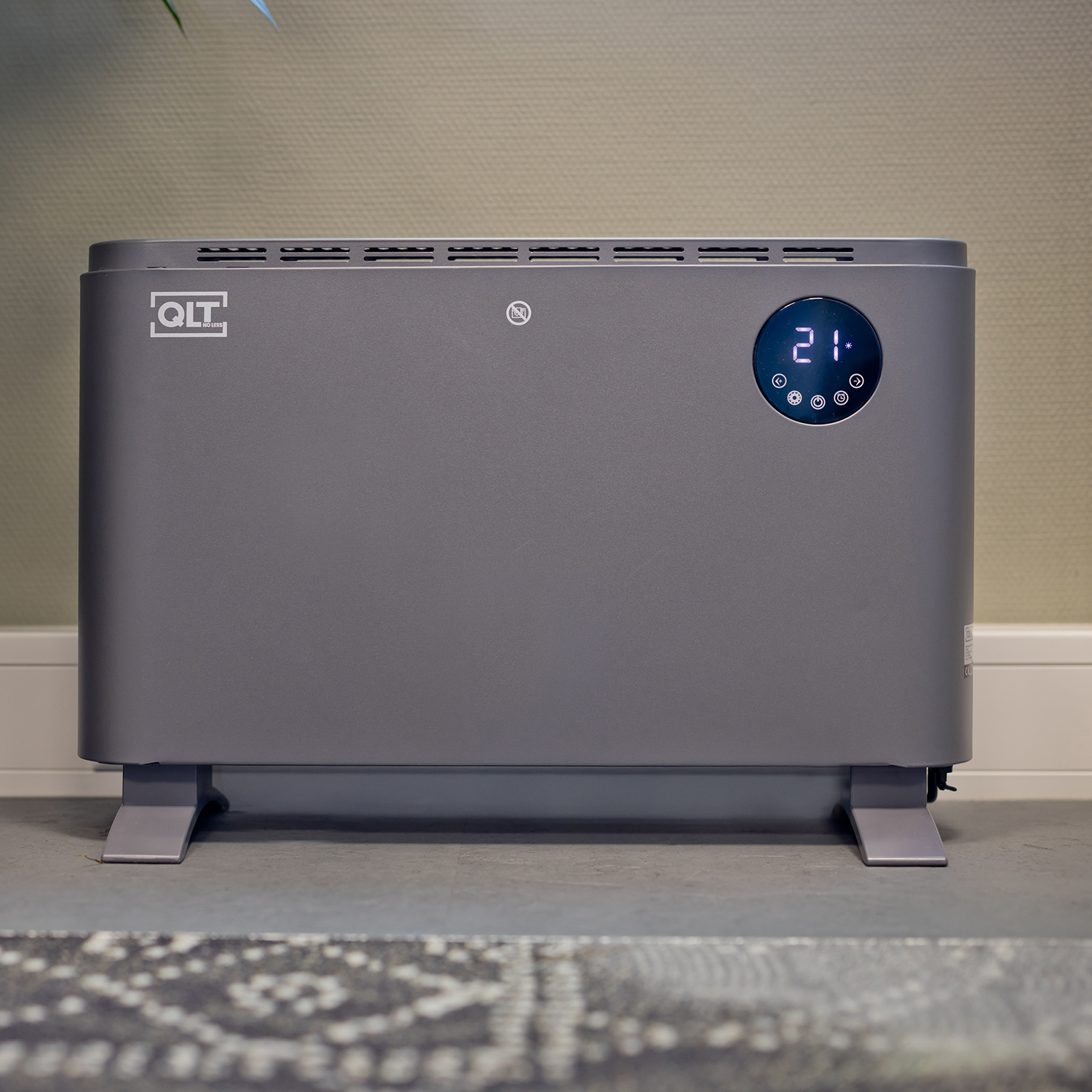 Een grijze elektrische kachel met een digitaal display. Staat op een grijs oppervlak, in een kamer.