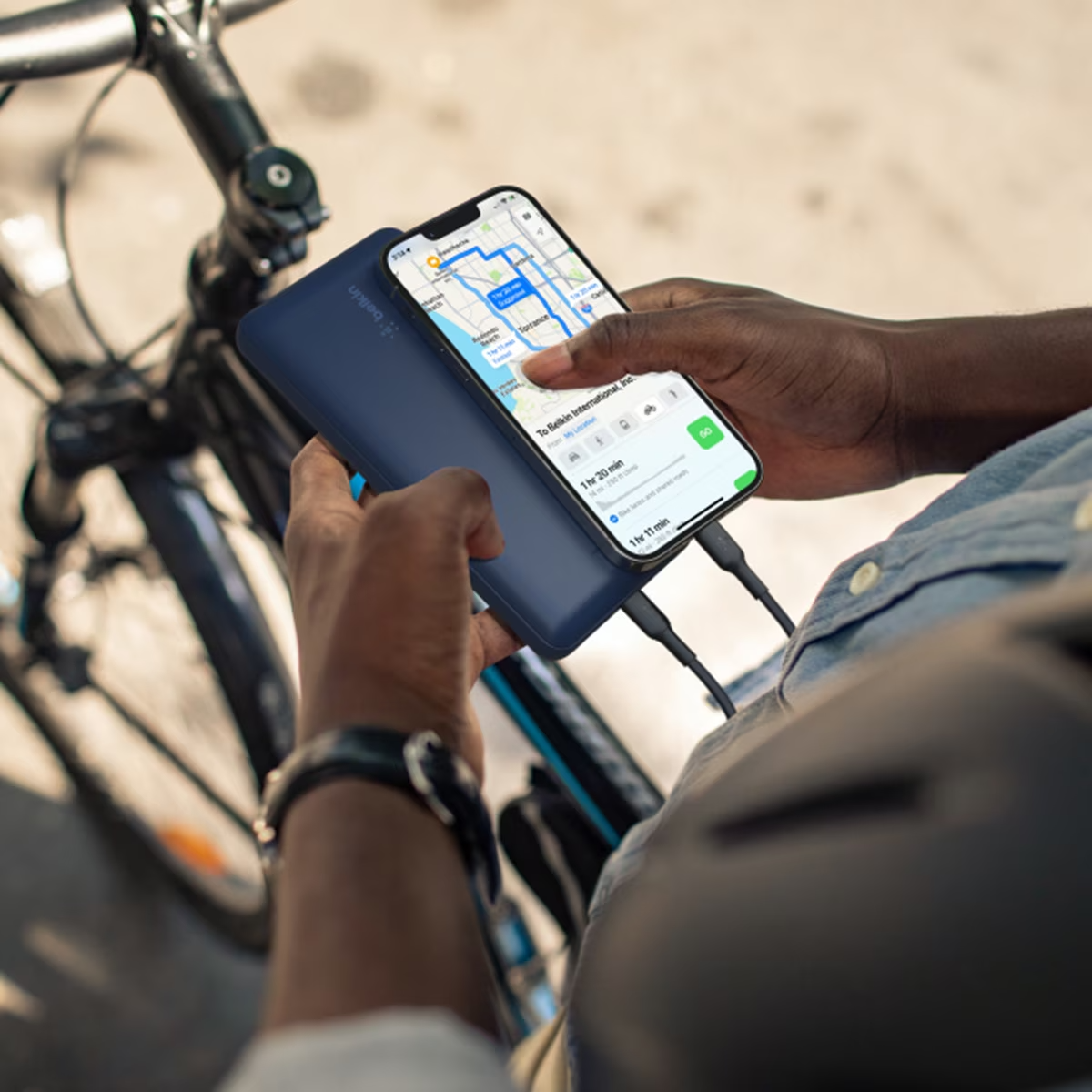 Una persona tiene in mano un telefono e un power bank. Il telefono mostra una mappa. Una bicicletta sullo sfondo.