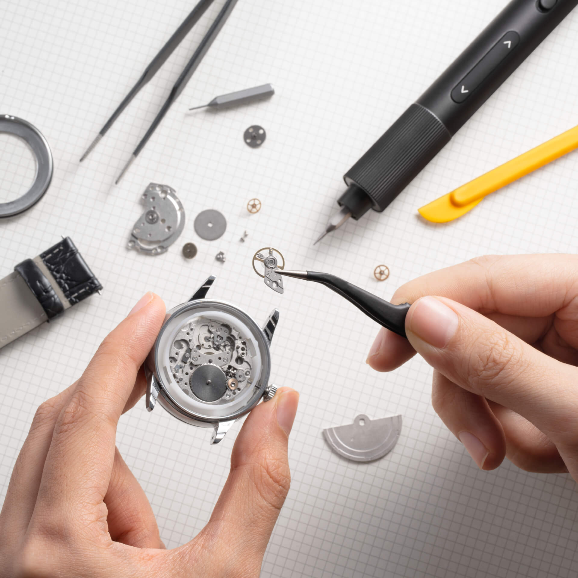 Nahaufnahme der Uhrenreparatur. Werkzeuge und Uhrenteile um eine zerlegte Uhr herum.
