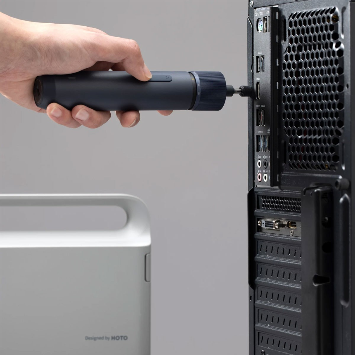 Eine Person, die einen dunkelblauen Schraubendreher an die Rückwand eines Computers anschließt, mit weißem Objekt.