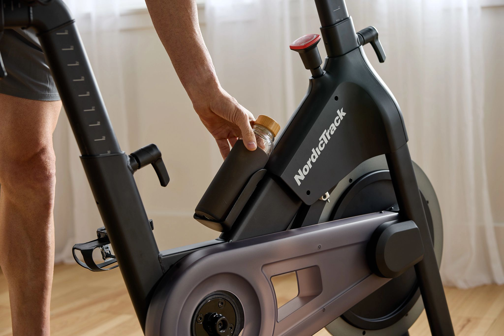 Eine Person, die eine Flasche in einen Flaschenhalter an einem schwarzen NordicTrack-Heimtrainer einlegt.