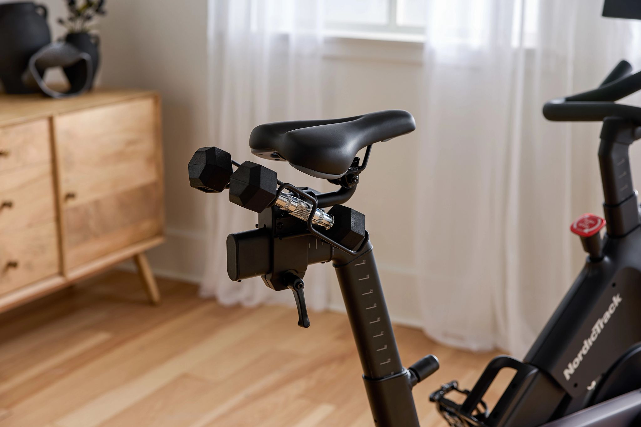 Heimtrainer mit Hanteln und Sattel. Fenster im Hintergrund mit Vorhängen, Holzschrank.