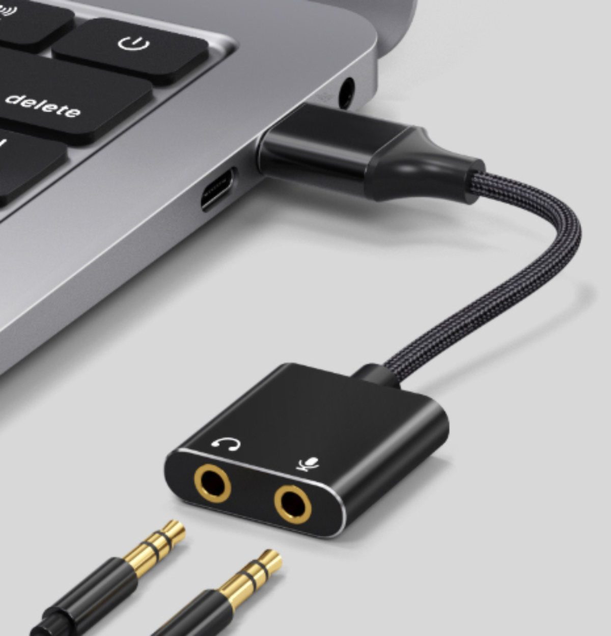 Ein schwarzer Adapter ist mit einem Laptop verbunden, mit Kopfhörer- und Mikrofonanschlüssen.