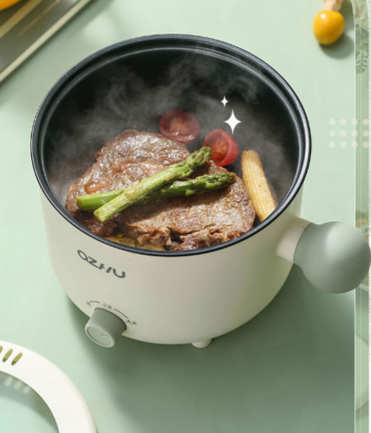 Ein kleiner, weißer Kochtopf mit Essen darin. Es kommt Dampf heraus. Spargel, Mais und Steak.