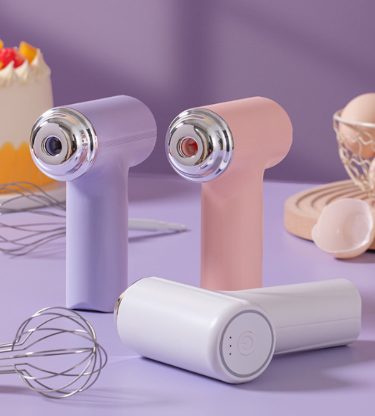 Drei kleine, kabellose Handmixer. Einer ist lila, einer rosa und der andere weiß. Auf einer lila Oberfläche platziert.