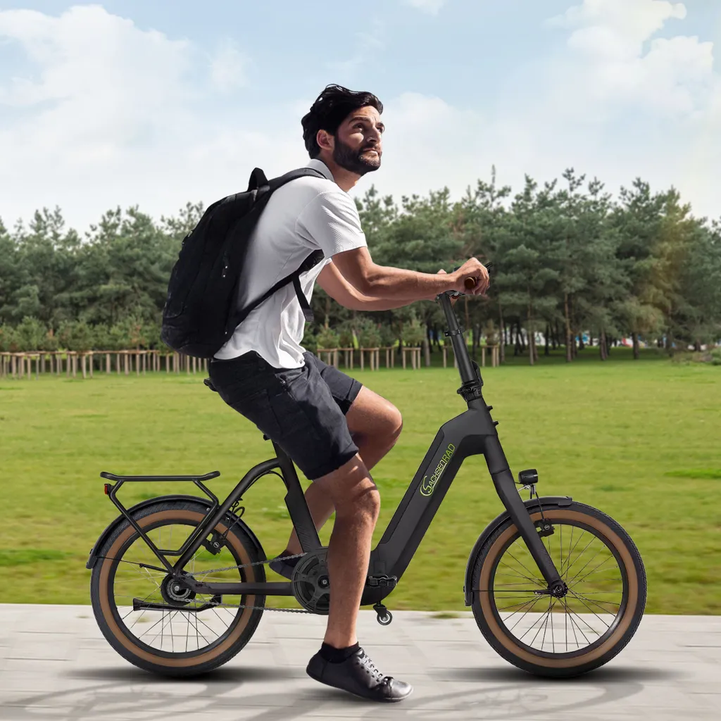 Mann fährt mit Rucksack auf einem schwarzen E-Bike. Grüne Bäume und Gras sind im Hintergrund.