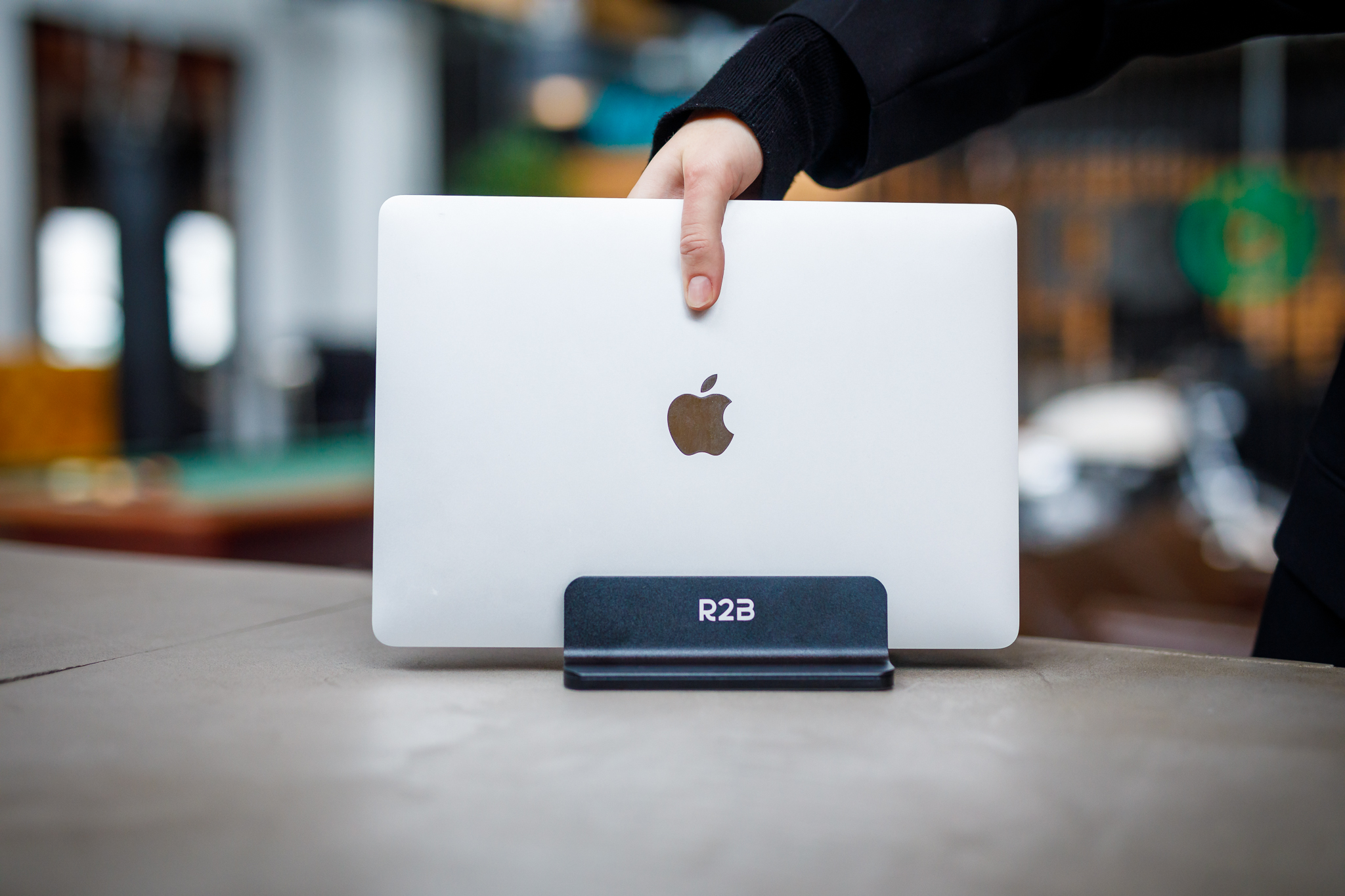 Eine Person, die einen silbernen Laptop mit Apple-Logo auf einem schwarzen Ständer hält.