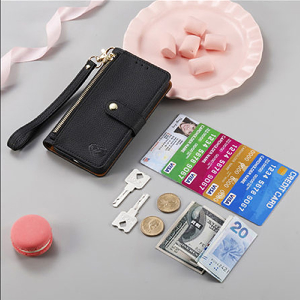 Un portafoglio nero con carte, chiavi, denaro e un piatto rosa con dolcetti.