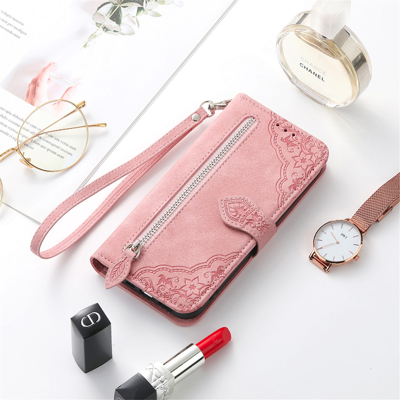 Custodia per telefono rosa a portafoglio con cerniera. Profumo, rossetto e orologio accanto. Sfondo bianco.