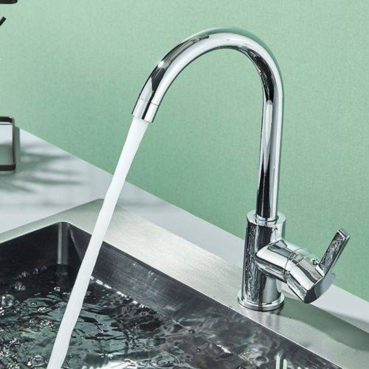 Ein verchromter Wasserhahn, aus dem Wasser in ein Waschbecken fließt. Der Hintergrund ist hellgrün.